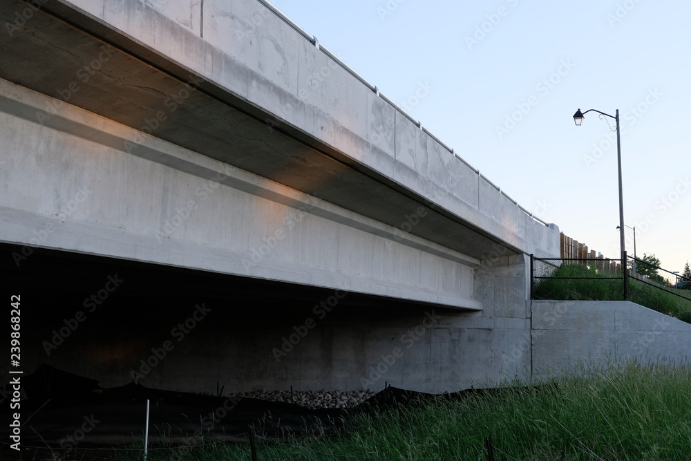 A Bridge Overpass with Grass Underneath. A Lamp Post is Beside the Road that the Bridge is Holding. A Bridge Overpass with Grass Underneath. A Lamp Post is Beside the Road that the Bridge is Holding.