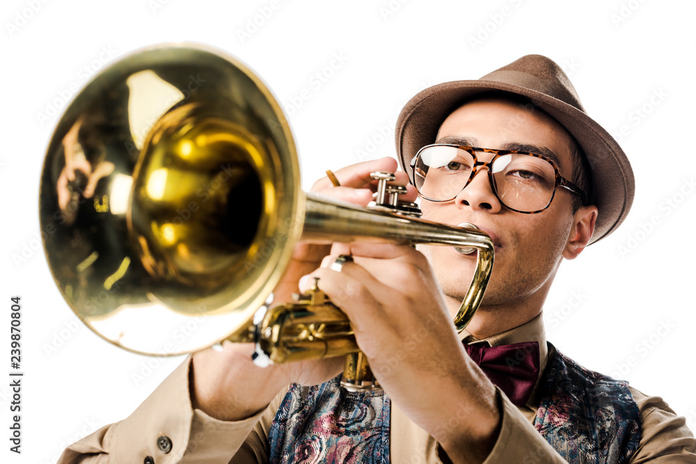 Obraz premium close up portrait of young mixed race man in stylish hat and eyeglasses playing on trumpet isolated on white