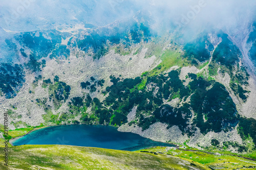 Beautiful foggy high mountains peaks  amazing lake  summertime. Alpine green fields  landscape.