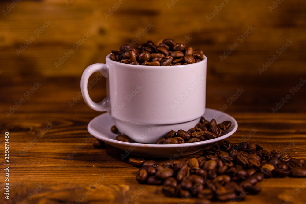 White cup filled with coffee beans on wooden table