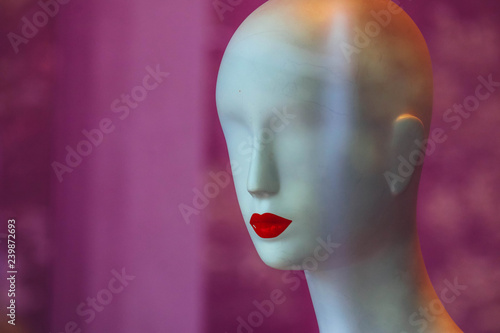 A bold white female mannequin with no eyes and red lips in a showcase of the fashion store on a black background.