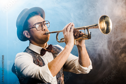 Photography stylish jazzman in hat and eyeglasses playing on trumpet on stage with dramatic