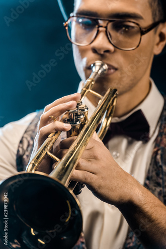 selective focus of young jazzman playing on trumpet on stage with dramatic lighting and smoke
