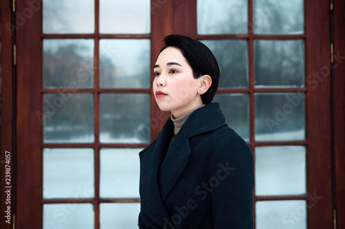 Close up portrait of trendy stylish hipster girl with short hair style in city street. Elegant millennial young woman wearing blue coat in cool winter day. 