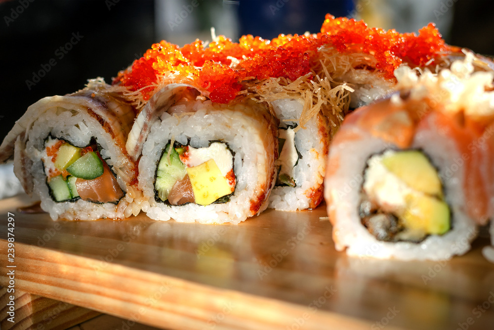Traditional seafood in Asia or Japan. Maki sushi rolls sprinkled with flying fish roe lie on a wooden table. Traditional seafood in Asia or Japan. Maki sushi rolls sprinkled with flying fish roe lie on a wooden table.