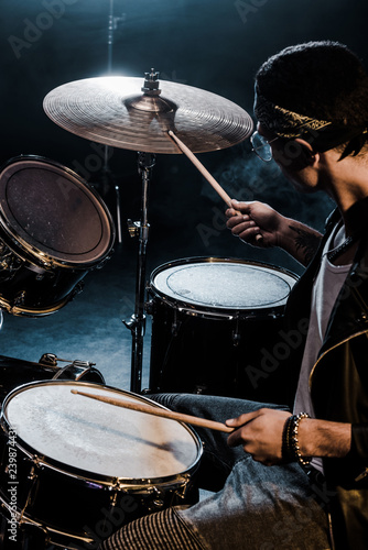 side view mixed race male musician playing drums during rock concert on stage