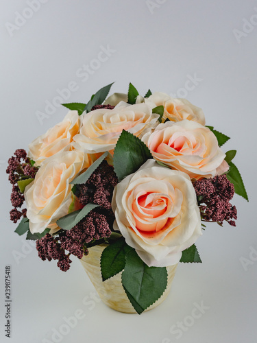 peach-colored artificial roses in a patinated pot on a white background