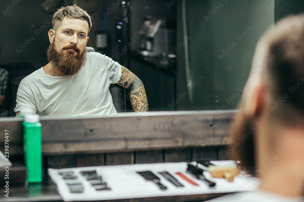 Tattooed man sitting and looking at his reflection in the mirror Tattooed man sitting and looking at his reflection in the mirror