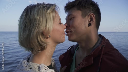 Multi ethnic young kissing interracial couple outdoors. Asian guy and caucasian girl on a date. Beautiful interracial couple in casual wear is relaxing in nature and spending time together. Tender