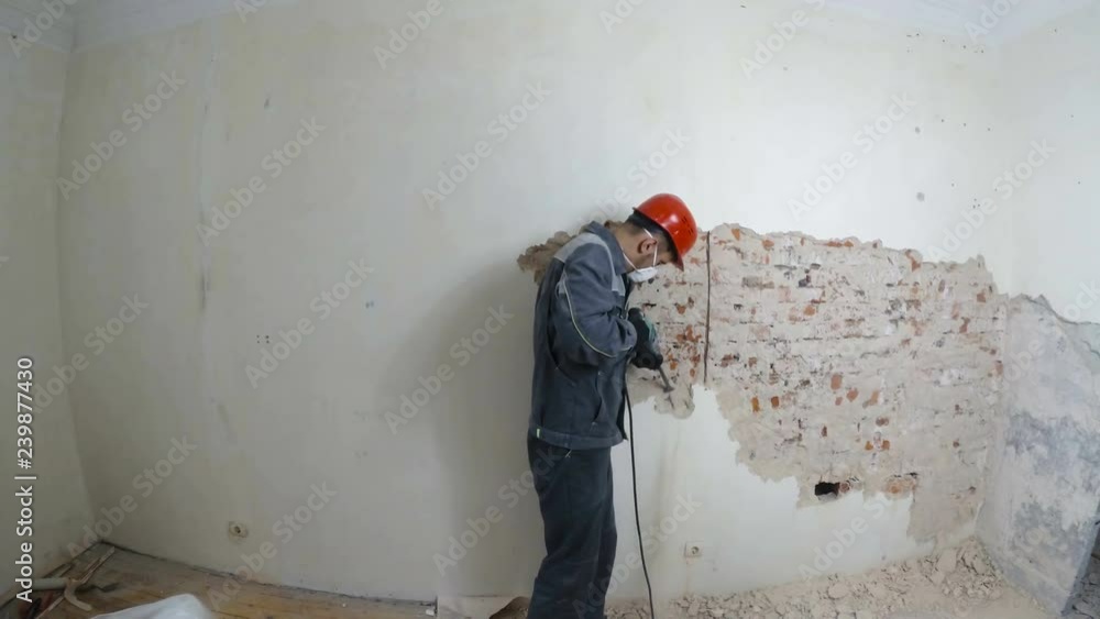 worker in protective suit demolishes plaster wall. Dirty, hard work. Personal protective equipment. Helmet, respirator and goggles. worker in protective suit demolishes plaster wall. Dirty, hard work. Personal protective equipment. Helmet, respirator and goggles.