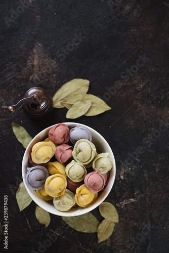 Bowl of raw multicolored dumplings or pelmeni over dark brown stone background, flatlay, copy space