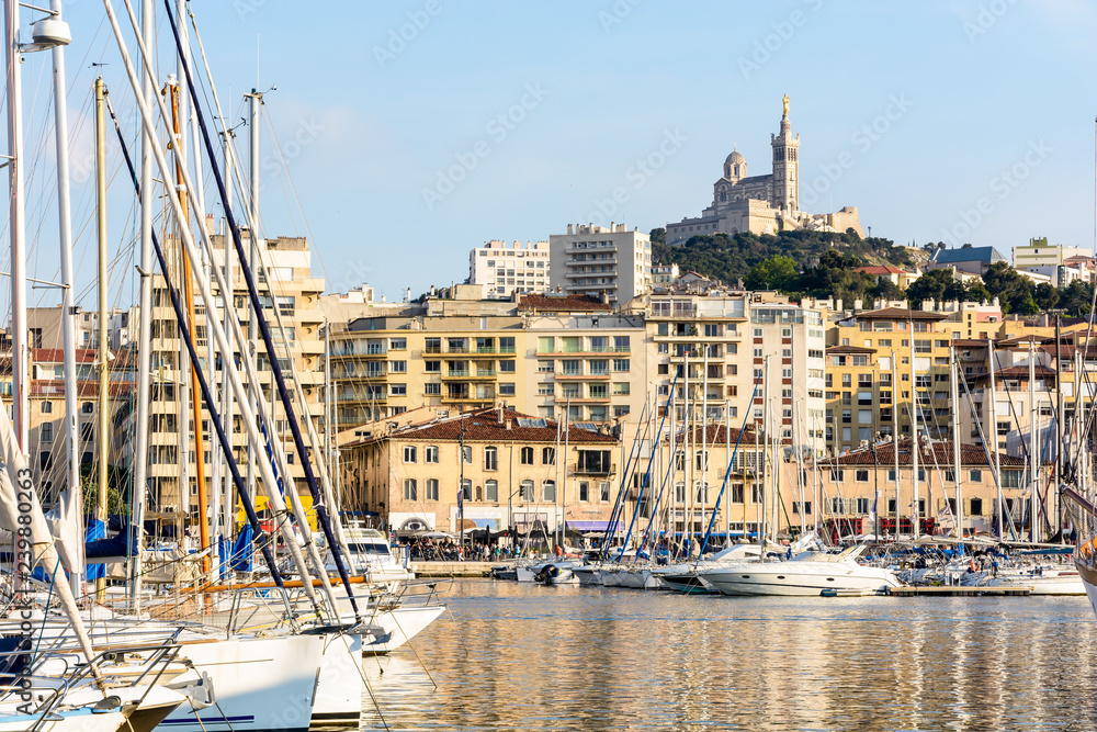 Φωτογραφία The Old Port of Marseille, France, with motorboats and sailboats moored in the marina and Notre-Dame de la Garde basilica on top of the hill at sunset
