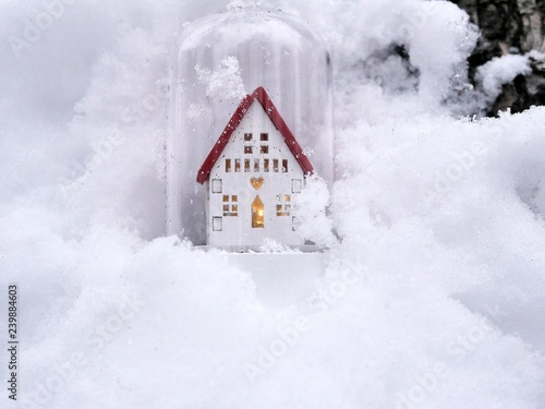 Small toy decorative white house with a red roof and lighted illumination on a snow-covered tree  the concept of winter seasonal holidays  Christmas  a new home in the new year  home comfort