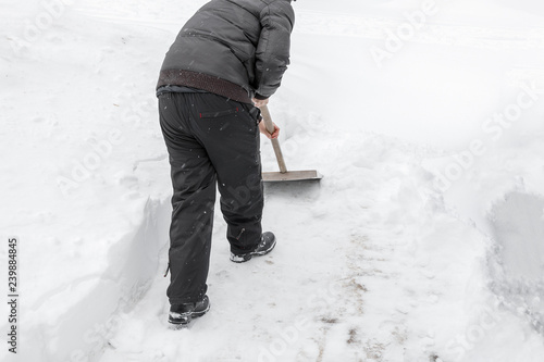 A man cleans snow shovel near the house