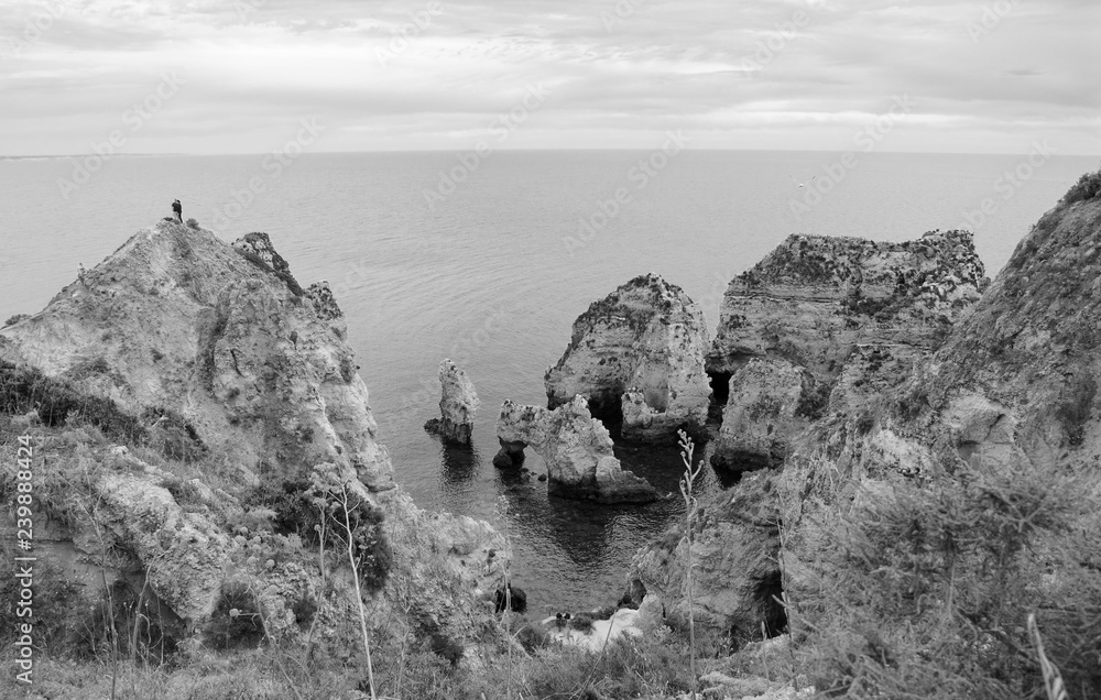 Unique stone arches, caves, rock formations at Dona Ana Beach (Lagos, Algarve coast, Portugal) in the evening light. Black white photo.