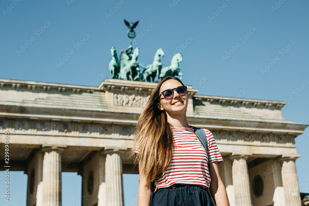 Portrait of a young beautiful positive smiling stylish tourist girl near the Brandenburg Gate in Berlin in Germany.