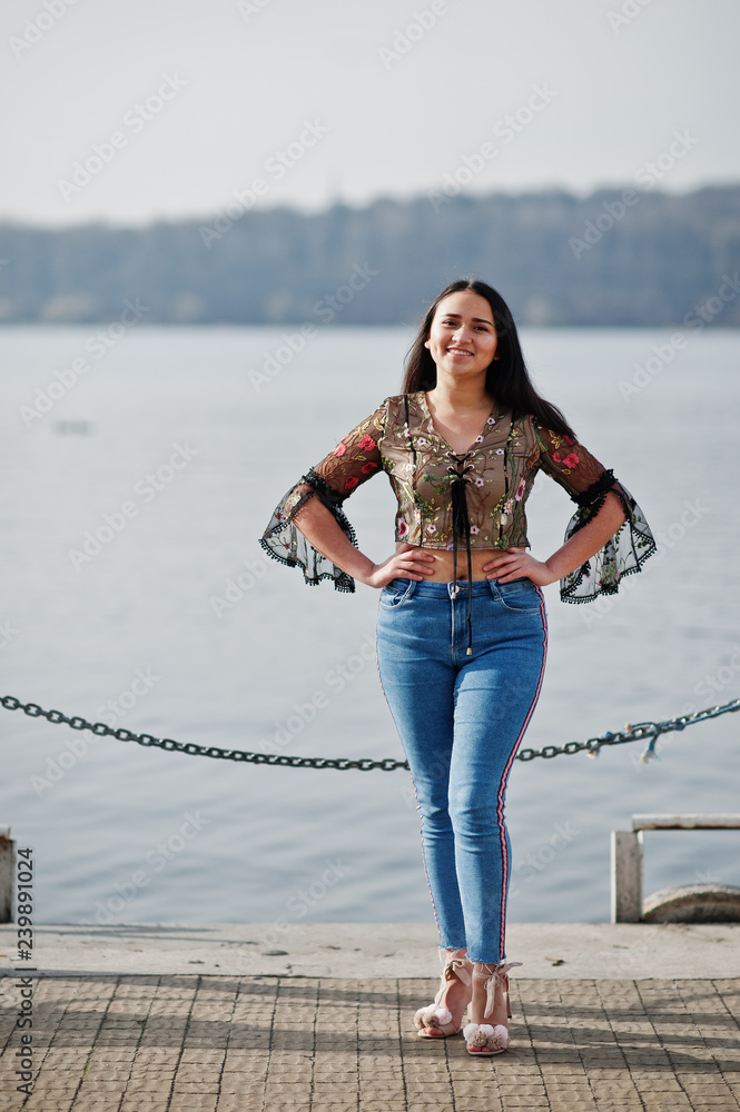 Pretty latino model girl from Ecuador wear on jeans posed against lake.  Stock Photo | Adobe Stock
