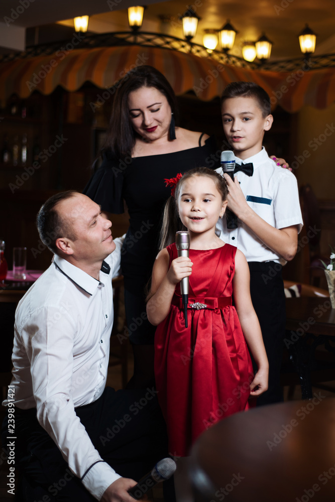 Fototapeta premium Little girl sings into a microphone in a circle of a happy family.
