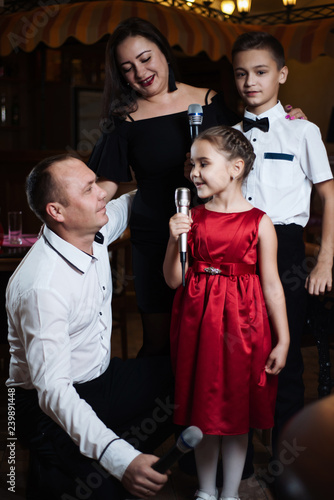 Little girl sings into a microphone in a circle of a happy family.