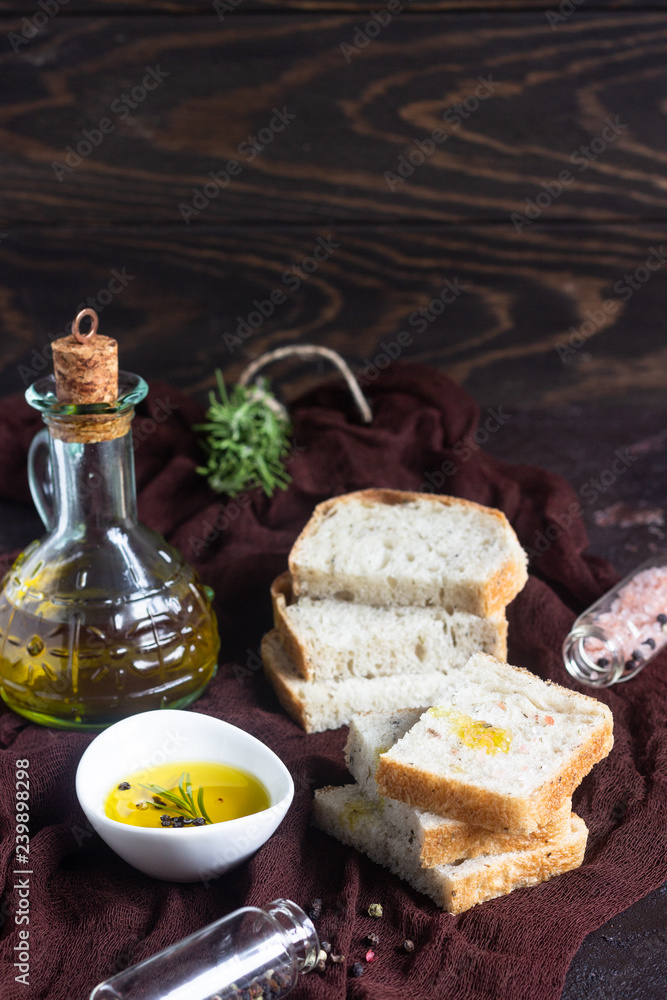 Sliced fresh bread and extra virgin olive oil on dark brown background 
