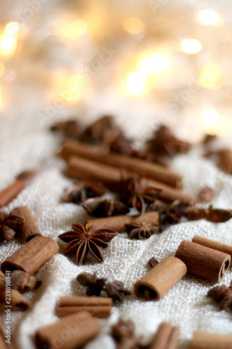 Cinnamon sticks and anise on beige tablelcloth. Fairy lights in the background. Selective focus.