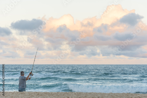 Man alone fishing with a rod in the Campeche Beach, in Florianopolis, Brazil.