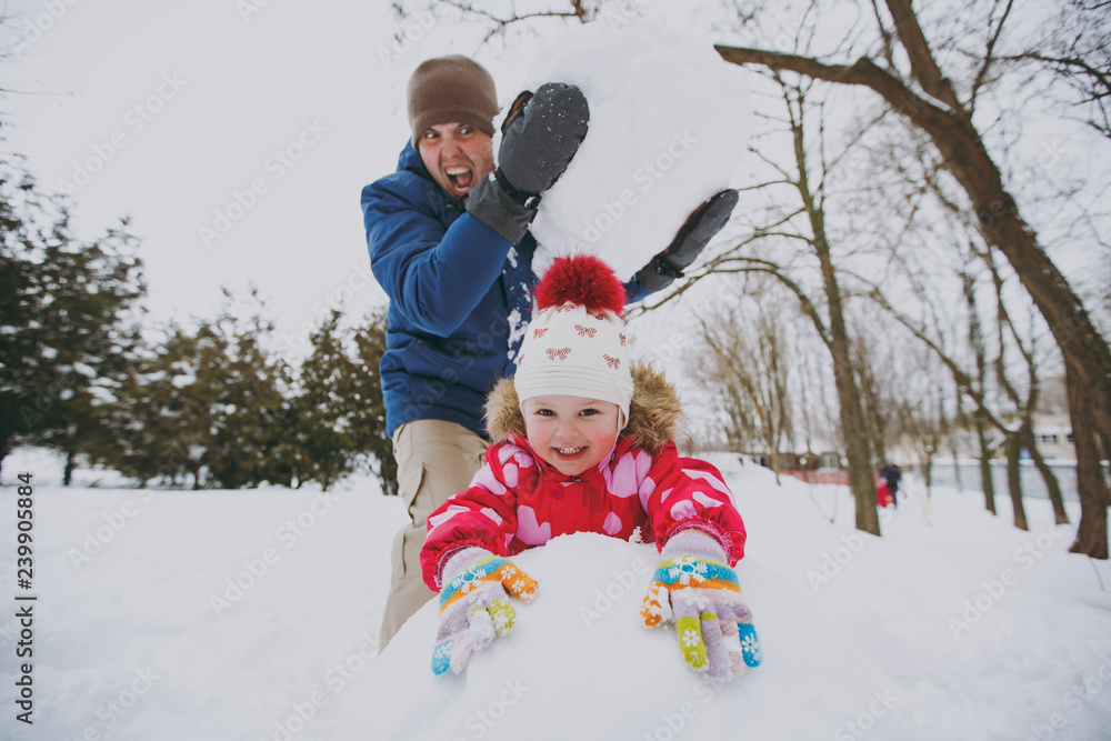 Funny family screaming dad in warm clothes holding big snowball, little girl playing with snow in park or forest outdoors. Winter fun, leisure on holidays. Love relationship family lifestyle concept.