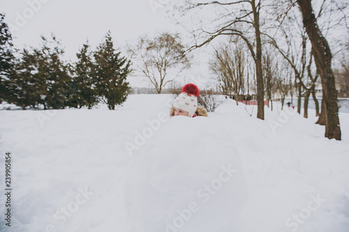 Pretty little girl in winter warm clothes and hat playing, hiding behind snowball in snowy park or forest outdoors. Winter fun, leisure on holidays. Love relationship family people lifestyle concept. © ViDi Studio
