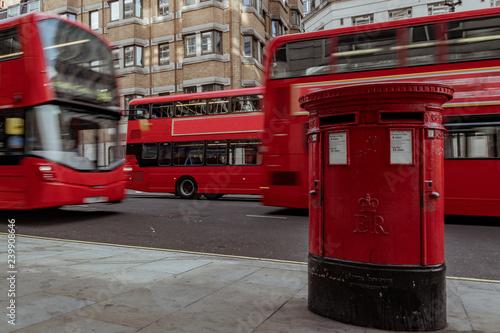 red mailbox in London with double decker bus passing by