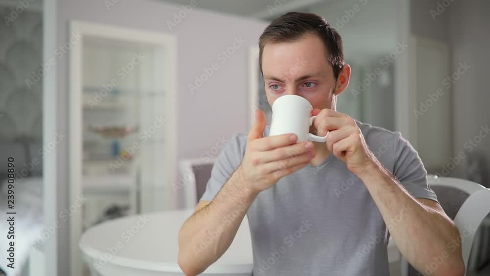 Young funny man drinking tea at home kitchen, turn face and smiling at camera Young funny man drinking tea at home kitchen, turn face and smiling at camera