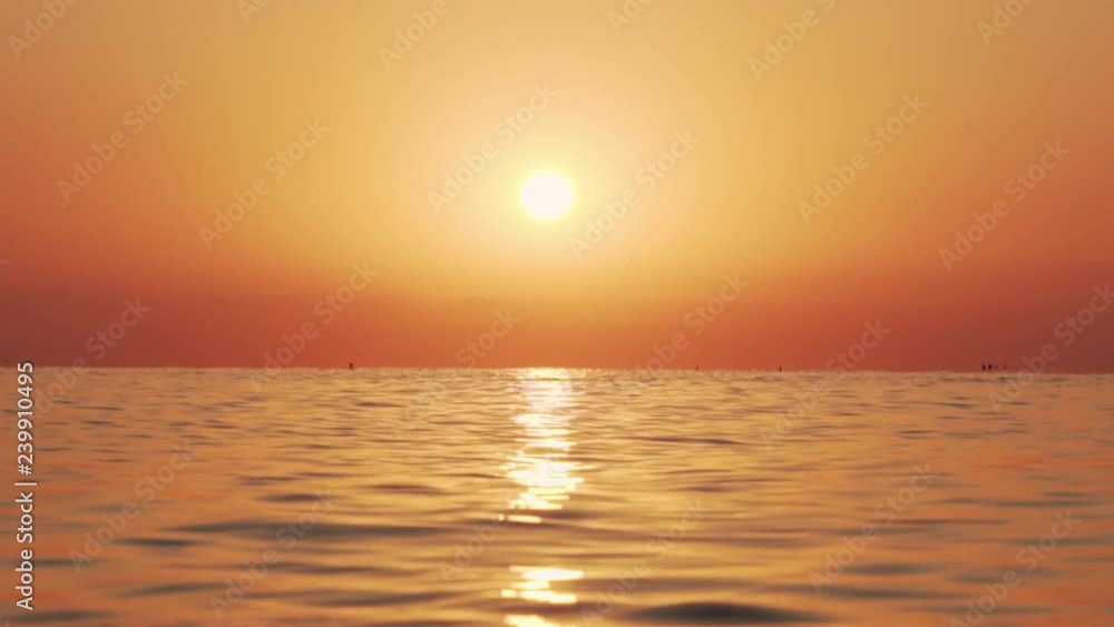 Slow motion of the sea surface with small waves against the backdrop of the sunrise of the sun. A large disk of the sun rises above the sea, a solar path on the water. Golden light of the sea panorama Slow motion of the sea surface with small waves against the backdrop of the sunrise of the sun. A large disk of the sun rises above the sea, a solar path on the water. Golden light of the sea panorama