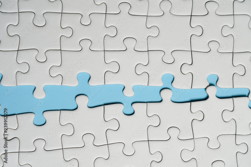Fragment of a folded white jigsaw puzzle and a pile of uncombed puzzle elements against the background of a blue surface. Fragment of a folded white jigsaw puzzle and a pile of uncombed puzzle elements against the background of a blue surface.