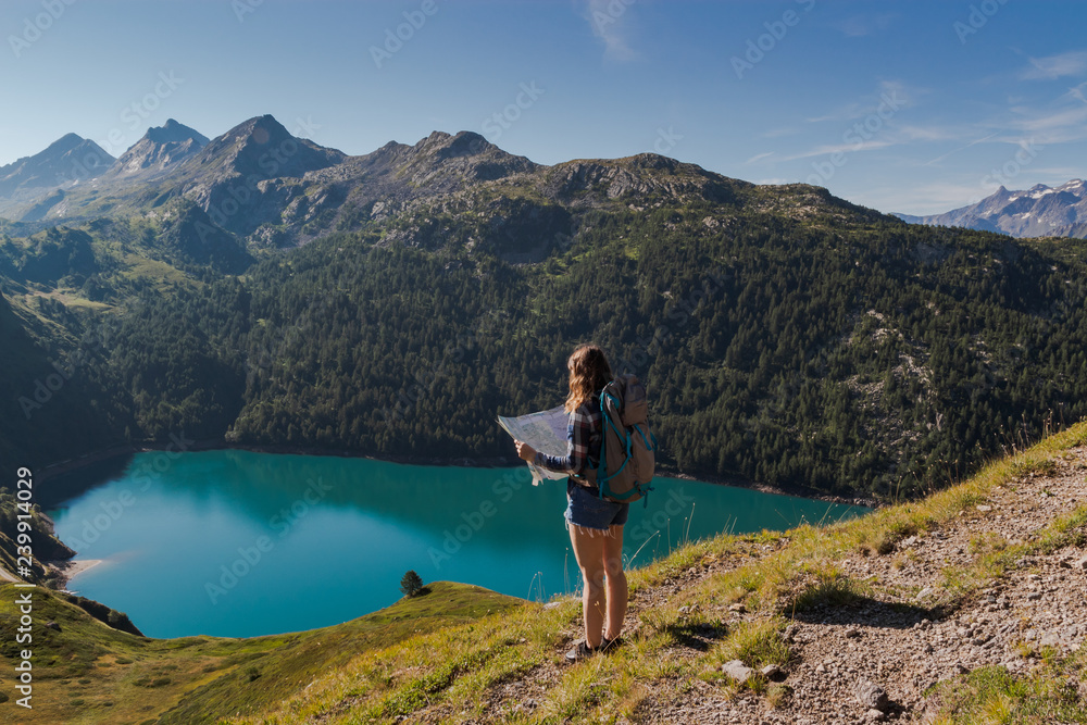 Young woman with backpack reading a map in the swiss alps. Lake ritom as background