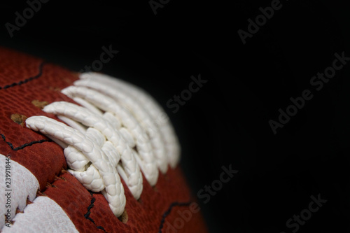 An American football game ball is shown up close, with the focus showing the detail of the laces, stitching, and surface. A black area for copyspace / text space is to the right.