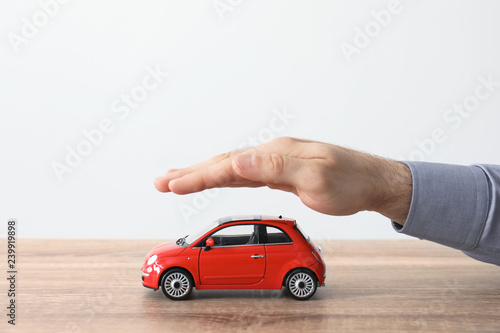 Male insurance agent covering toy car at table, closeup