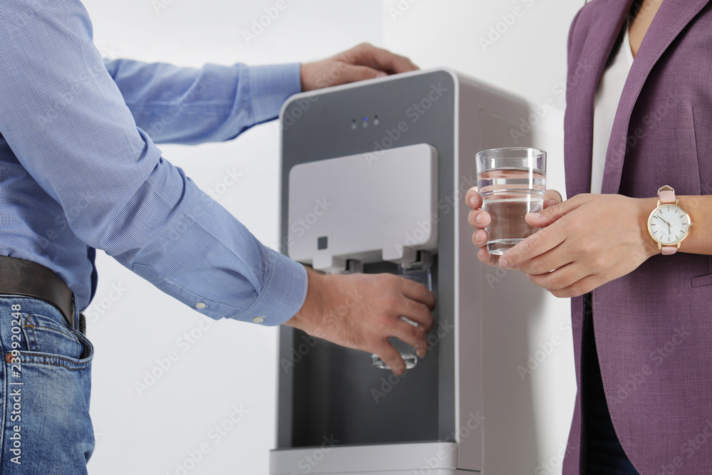 Employees taking glasses of water from cooler in office, closeup