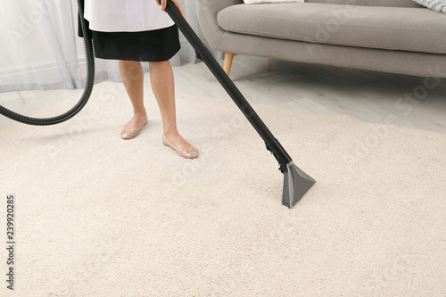 Chambermaid removing dirt from carpet with vacuum cleaner indoors, closeup. Space for text