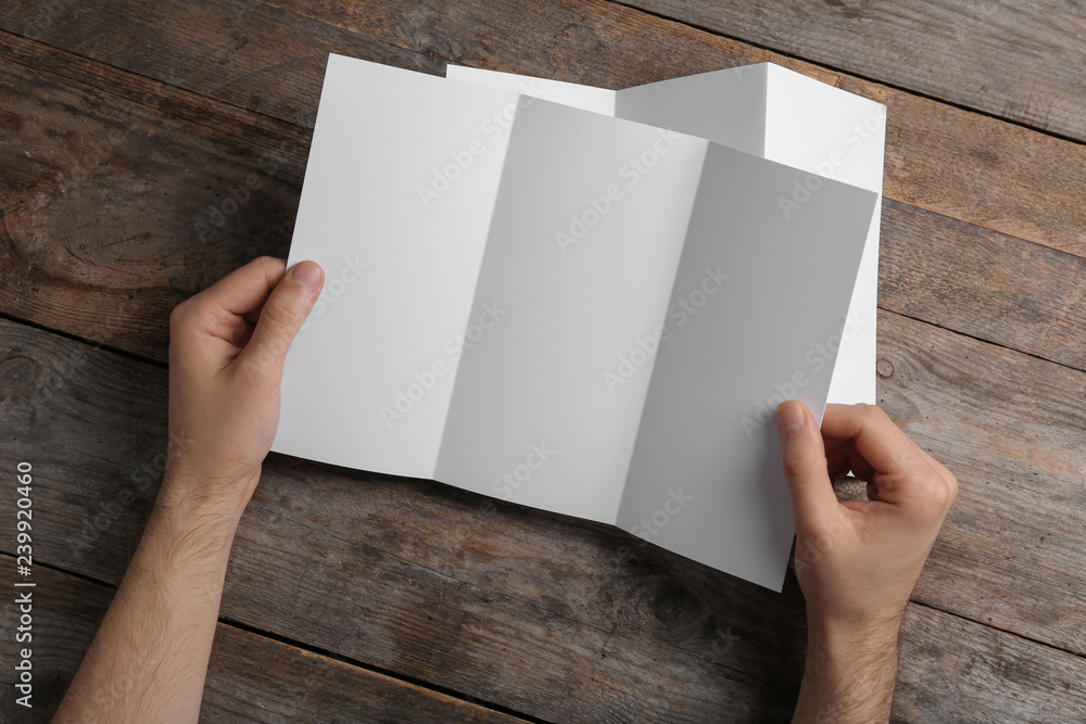 Man with blank brochure on wooden background, above view. Mock up for design Man with blank brochure on wooden background, above view. Mock up for design