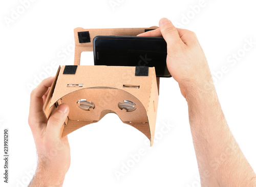 Man putting smartphone into cardboard virtual reality headset on white background, closeup