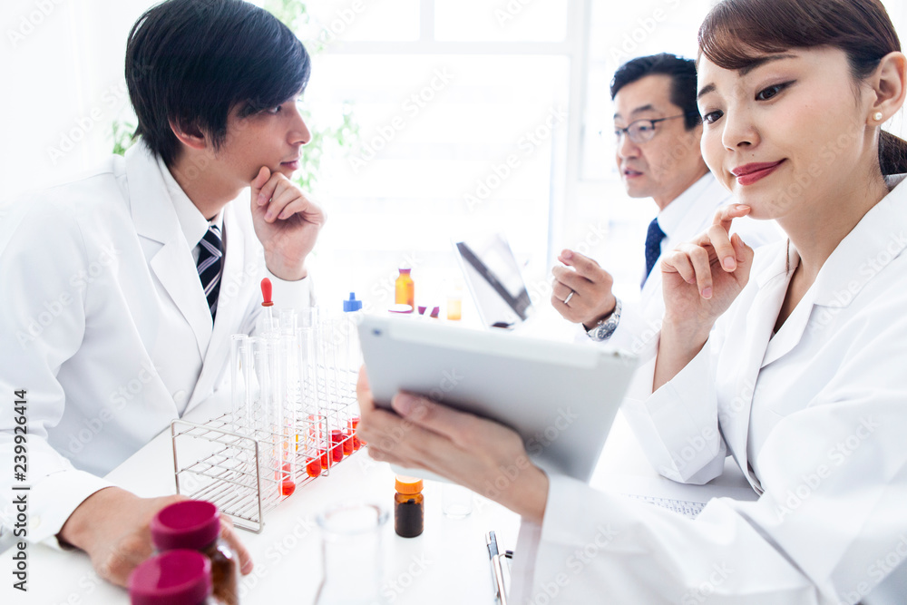 タブレットの表示を確認する女性研究員と議論をする男性研究員たち タブレットの表示を確認する女性研究員と議論をする男性研究員たち