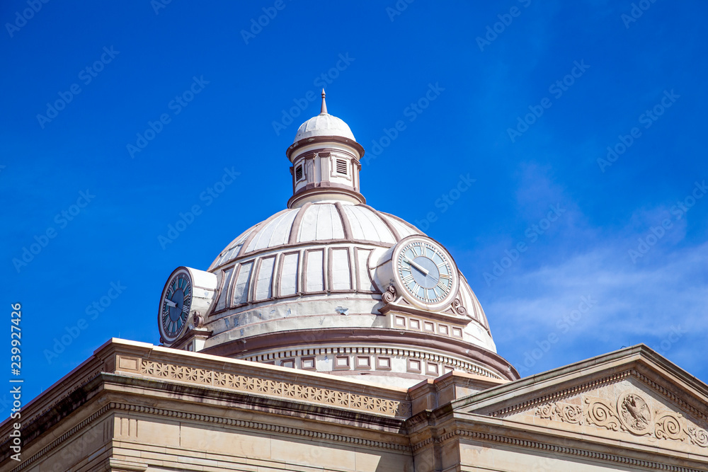 Decorative dome on a city hall building with clock and blue sky in the background