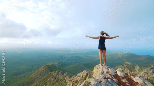 Young woman with arms raised at mountain peak overlooking jungle landscape