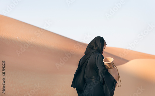 woman in abaya (emirati traditional dress) in a desert with water dish
