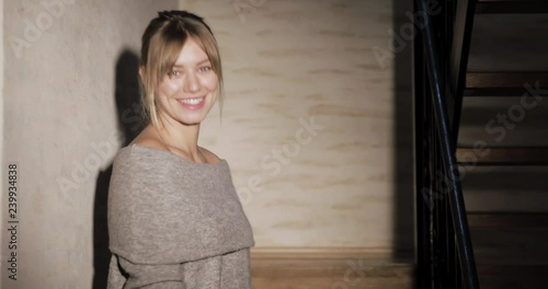 Beautiful blonde woman smiles at the camera and then goes upstairs