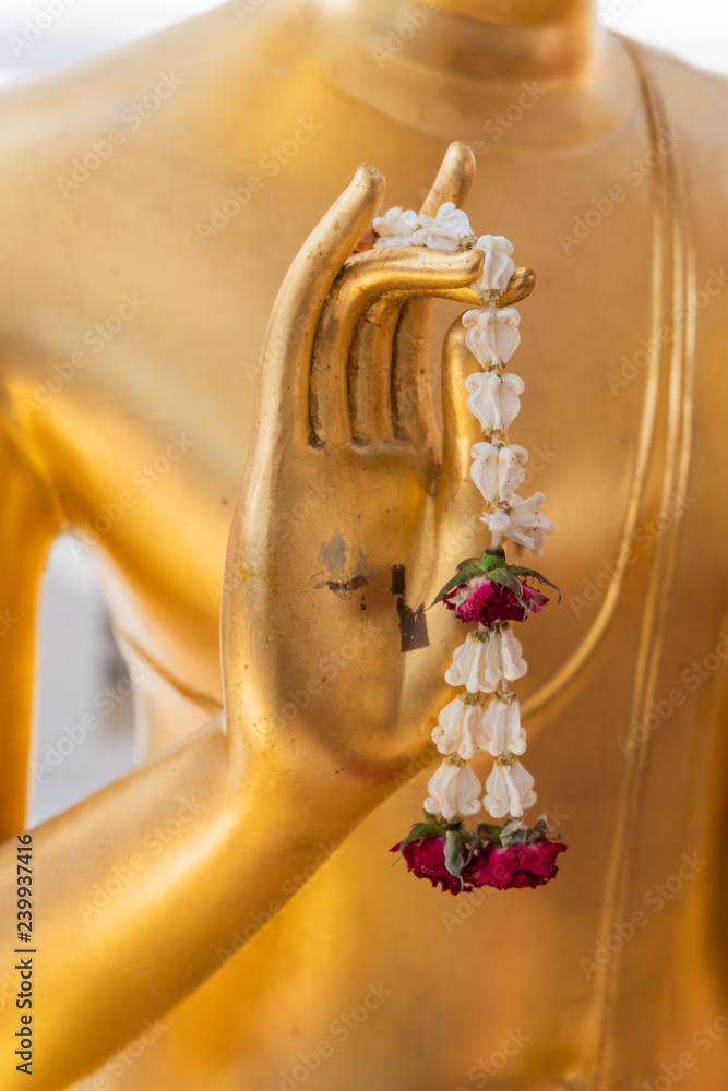 Naklejka premium Close up Hand of The Buddha statue gold color hold flower garland in temple at thailand