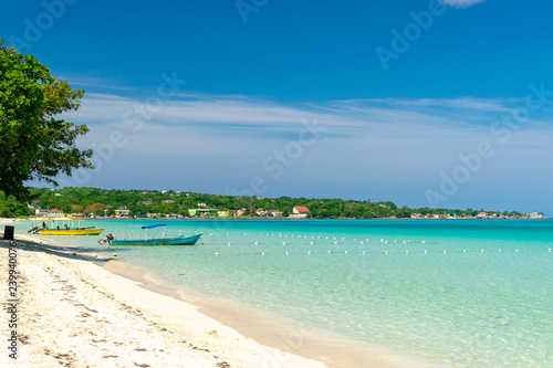 Sunny day along the Seven Mile Beach in tropical Negril  Jamaica. Tour boats await passengers and caucasian tourists in the water at a distance.