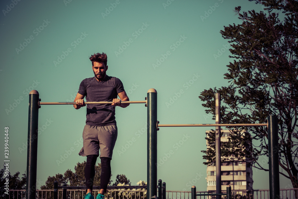 Young man exercising on gymnastic bar in park at morning