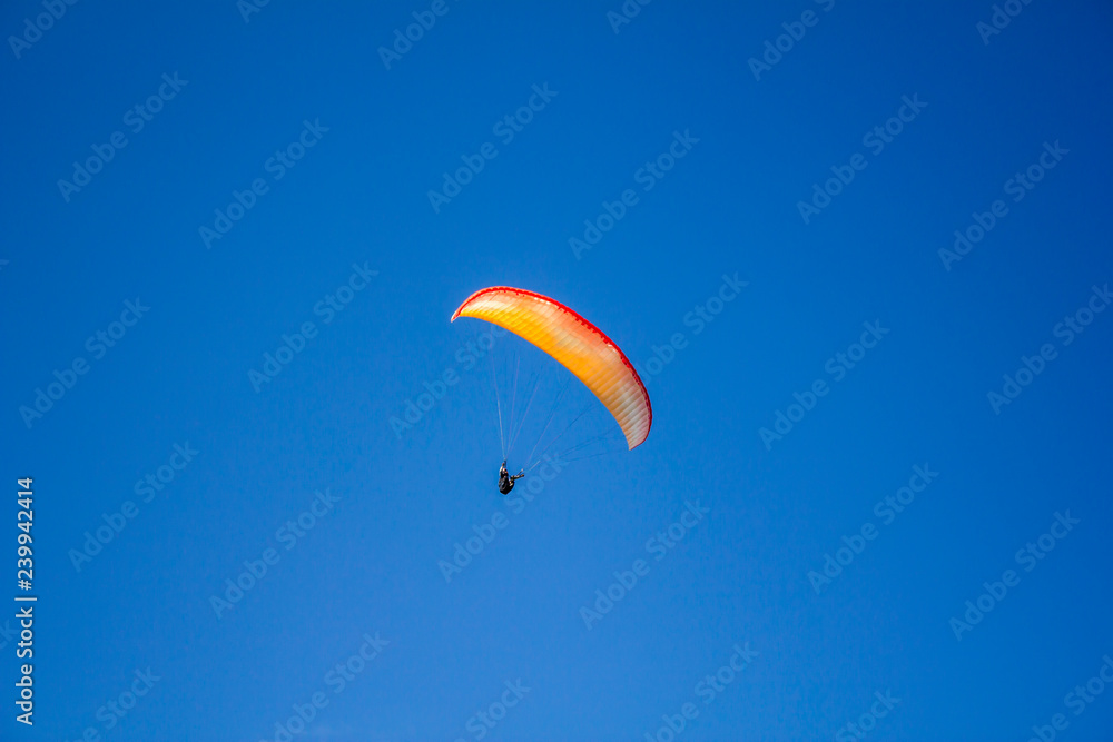 man on a red yellow white paraglide in a clear blue sky man on a red yellow white paraglide in a clear blue sky
