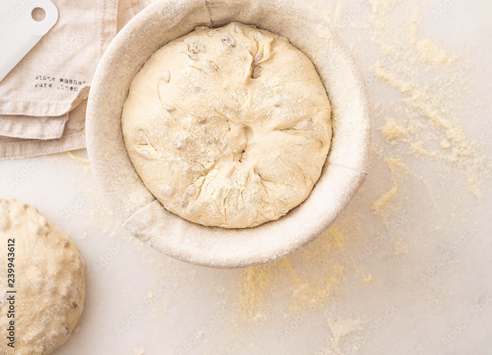 Baking bread. Dough in proofing basket on table with flour, sunflower seeds. Top view. Baking bread. Dough in proofing basket on table with flour, sunflower seeds. Top view.