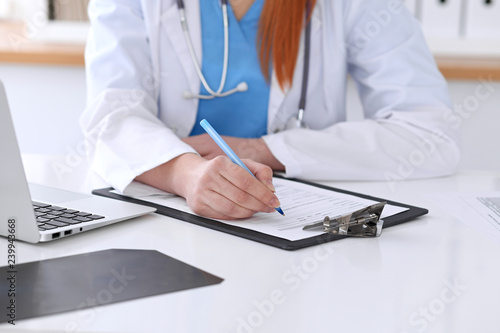 Close up of a female doctor filling up  an application form while sitting at the table